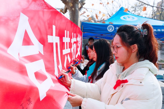 20231127中國石油大學(xué)（華東）青年學(xué)子在合力共抗艾滋的條幅上簽字，表達抗擊艾滋病的決心和信心  .jpg